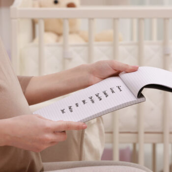 A woman reviewing unique baby names options on a notepad in front of a baby crib